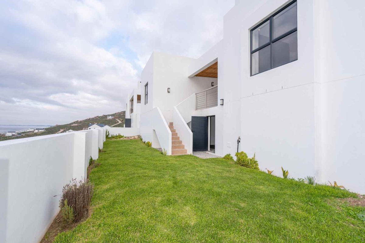 A modern white exterior rear facade featuring a landscaped lawn, external staircase, and balcony access, showcasing contemporary architectural design.