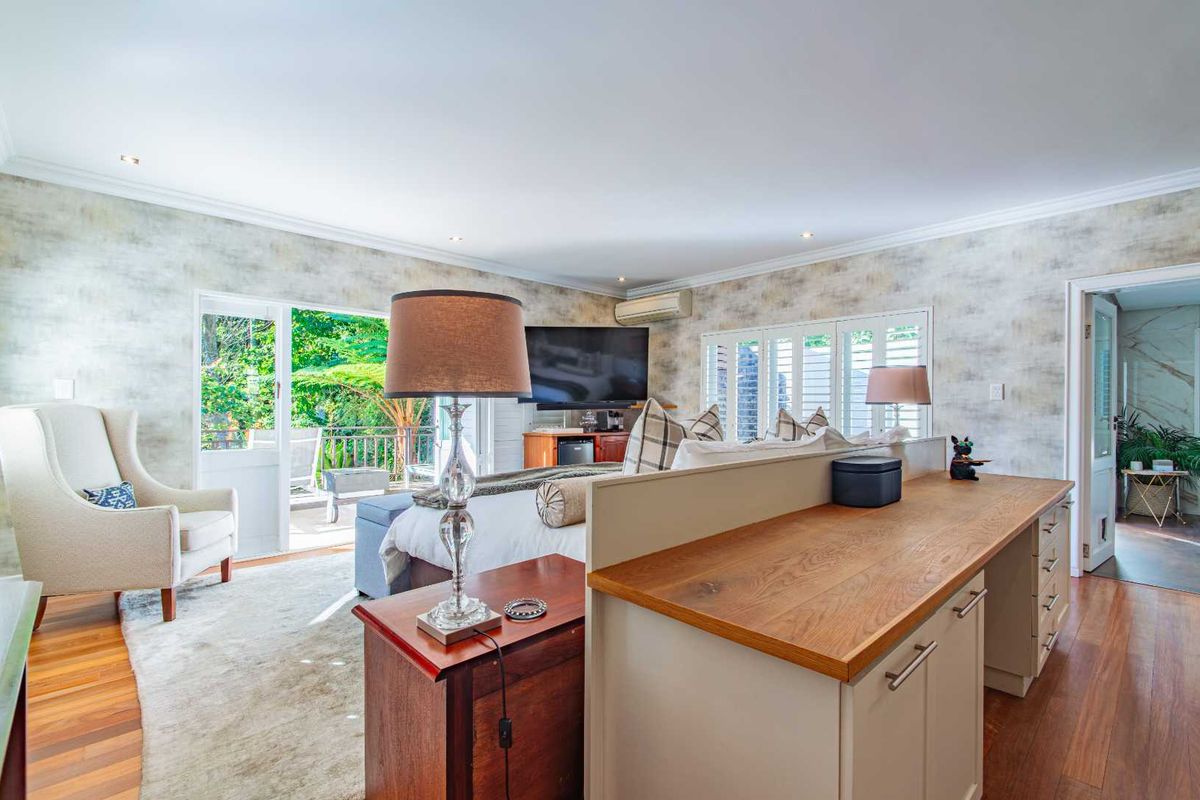Spacious bedroom featuring hardwood floors, built-in cabinetry with a timber countertop, plantation shutters, and direct access to an outdoor patio area.