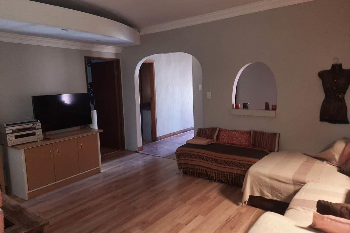 Spacious living room featuring light wood flooring, decorative ceiling coving, and arched wall openings leading to adjacent areas.