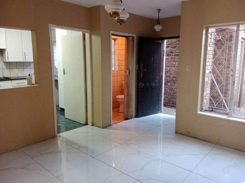 An empty living area featuring modern white tiled flooring, direct access to a bathroom and kitchen, and security-fitted windows and doors.