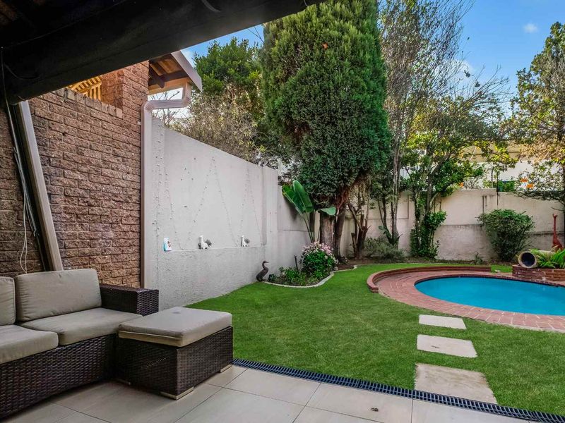 A private backyard featuring a swimming pool with brick coping, a tiled patio area, and a landscaped garden with established trees and boundary walls.