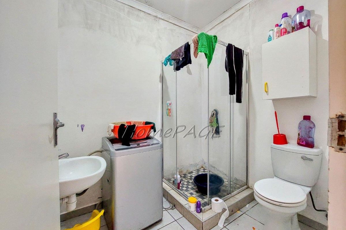A compact bathroom featuring a shower cubicle, toilet, and wall-mounted basin, requiring cosmetic updates and maintenance to the wall finishes.