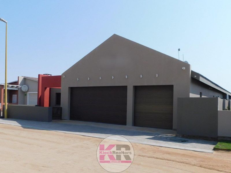 Front view of a modern house featuring a double garage with sectional doors, paved driveway, and contemporary exterior wall lighting.