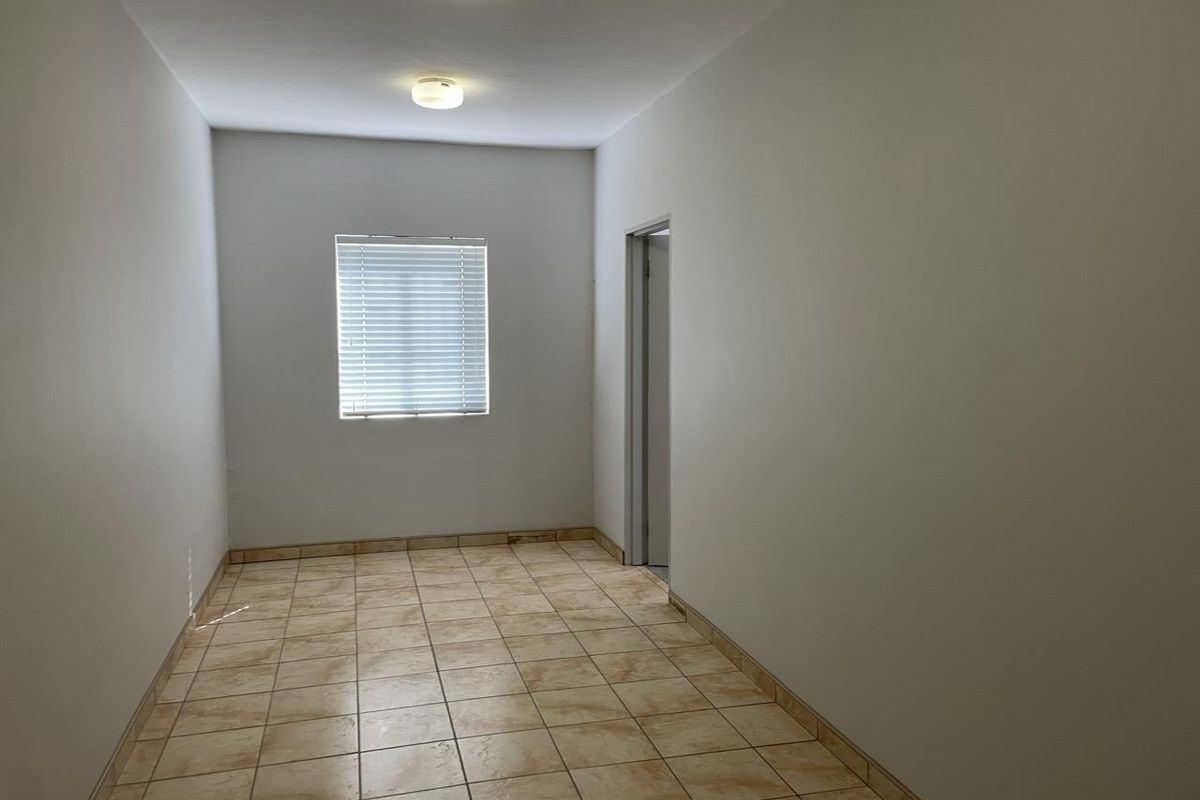 A clean, empty room featuring neutral tiled flooring, white walls, and a window fitted with horizontal blinds.