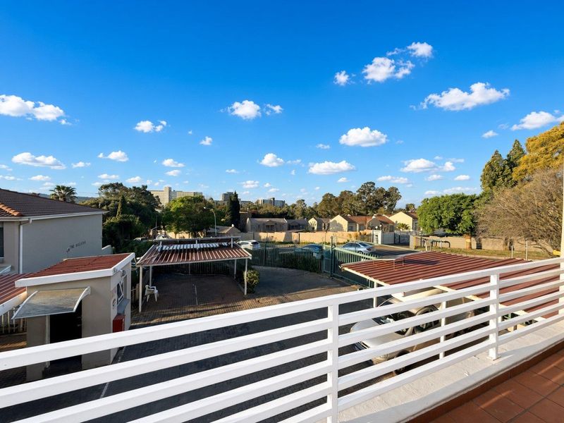 Elevated view from a balcony overlooking the complex driveway, carport parking areas, and surrounding neighborhood landscape.