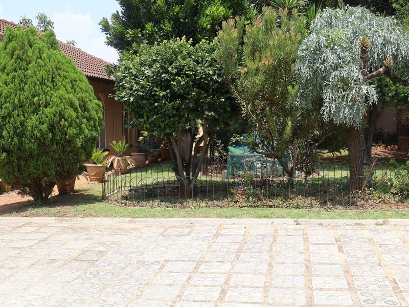 A view of the front garden area featuring established trees, shrubs, and a paved driveway leading to the house.