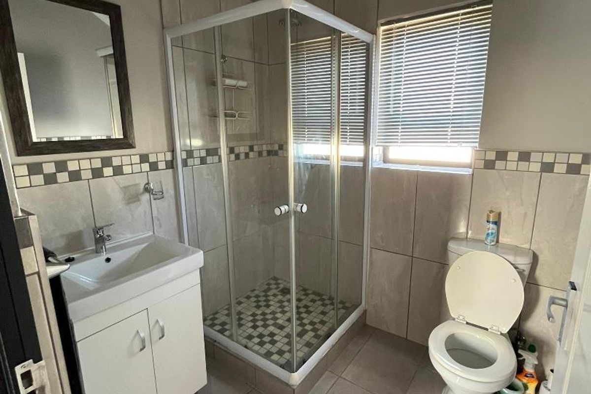 A functional bathroom featuring a glass-enclosed shower, a vanity basin with storage, and a toilet, finished with neutral wall and floor tiling.