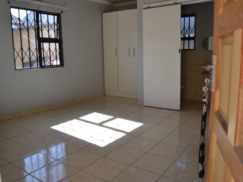 A bright, empty bedroom featuring tiled flooring, built-in cupboards, and a security gate on the window.