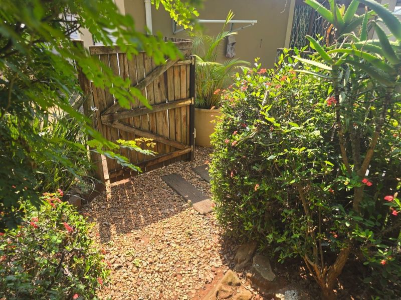 A private garden area featuring a gravel pathway, stepper stones, and a wooden access gate, complemented by established shrubbery and a wall-mounted clothesline.