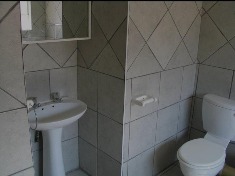A functional bathroom featuring a pedestal basin, toilet, and wall-mounted mirror cabinet, finished with neutral ceramic wall tiles.