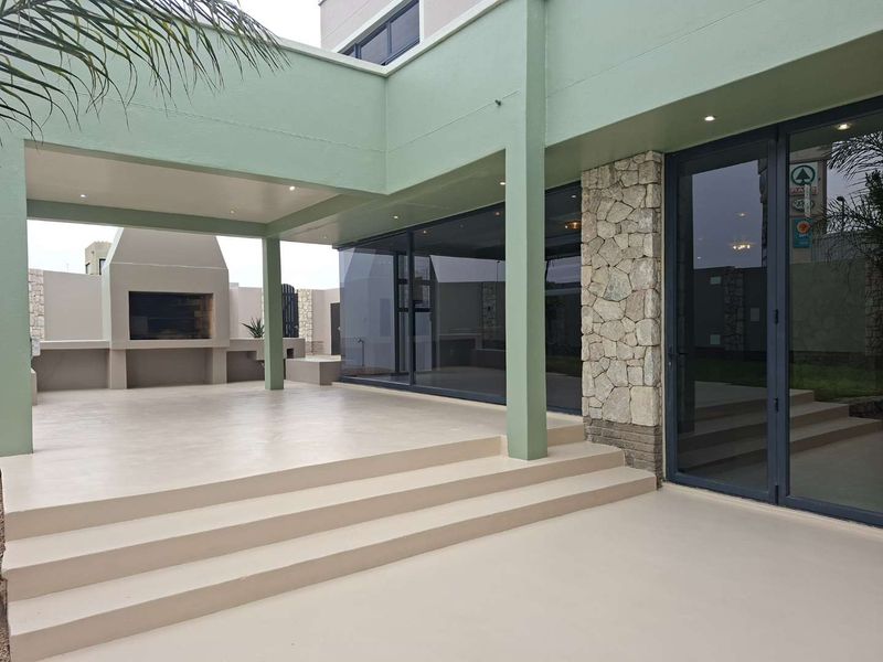 Spacious covered patio featuring a built-in braai, stone cladding accents, and large sliding glass doors leading into the home.