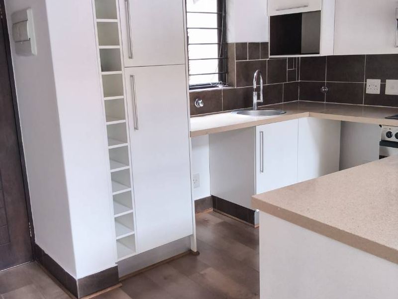 A functional kitchen featuring white cabinetry, laminate countertops, a tiled backsplash, and exposed timber ceiling beams, offering a clean and neutral workspace.