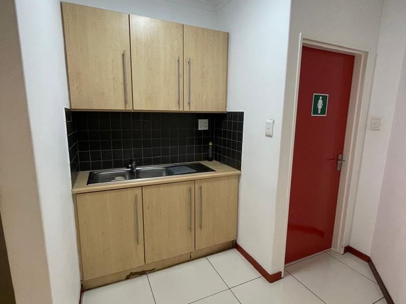 A functional scullery or kitchenette area featuring light wood cabinetry, a stainless steel sink, tiled backsplash, and tiled flooring.
