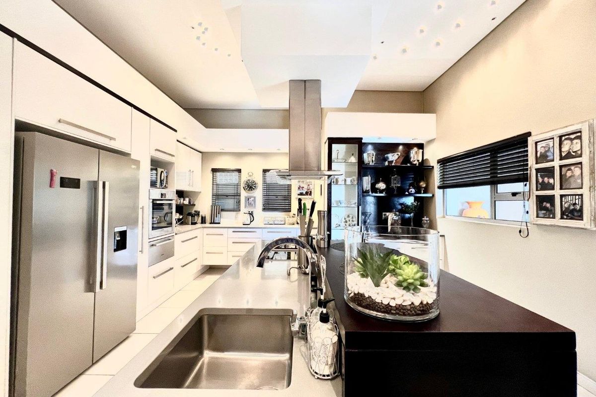 Modern kitchen featuring a large central island with a stainless steel sink, built-in appliances, and sleek cabinetry with recessed ceiling lighting.