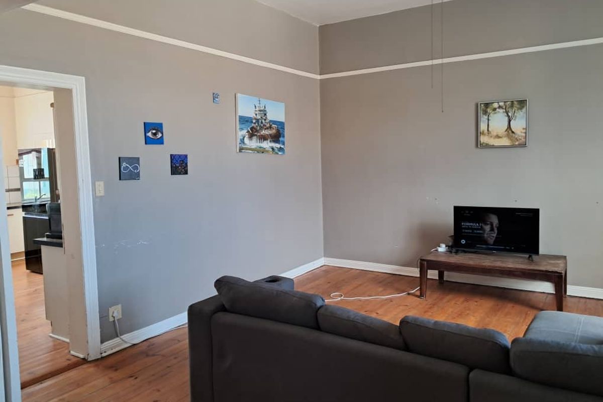 A living room featuring original timber flooring and neutral wall tones, with an open transition into the adjacent kitchen area.