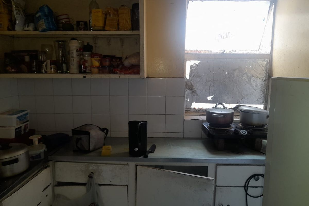 A dated kitchen area featuring built-in cabinetry, tiled splashbacks, and a window with a broken pane, requiring significant maintenance and renovation.