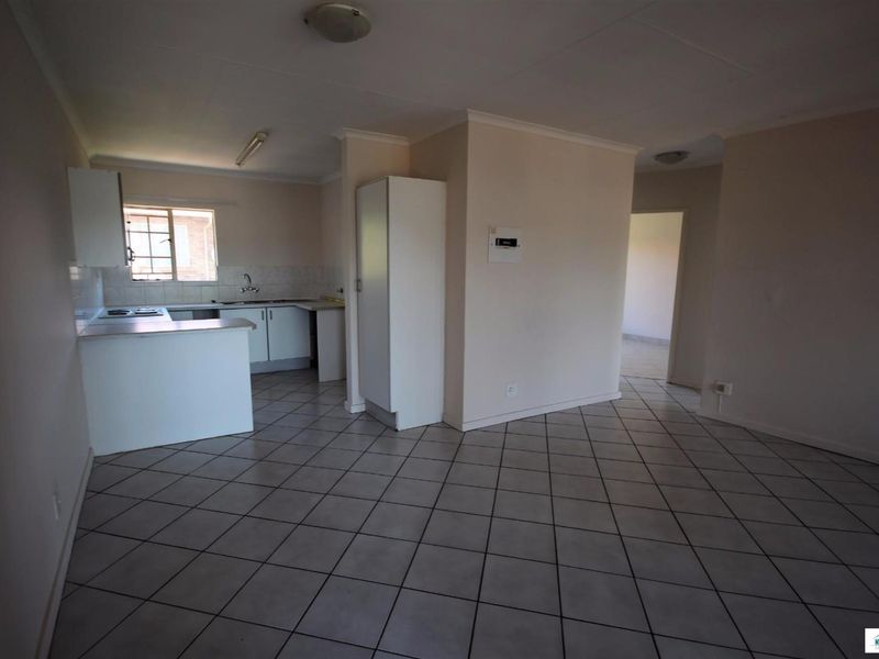 An open-plan living and kitchen area featuring tiled flooring, built-in cabinetry, and a breakfast counter in a neutral, vacant space.
