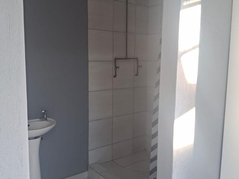 A functional bathroom featuring a pedestal basin and a tiled shower enclosure with exposed plumbing fixtures.