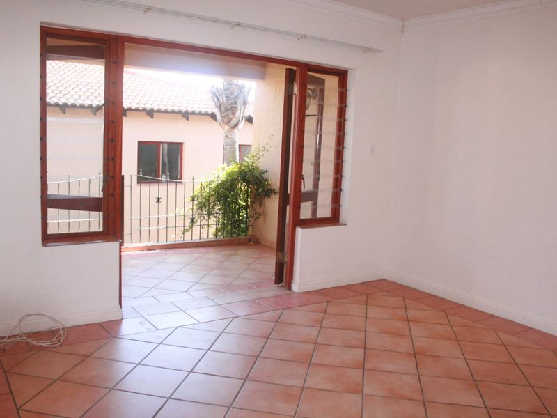 An empty living room featuring terracotta tiled flooring and large wooden-framed glass sliding doors that open onto a private balcony.