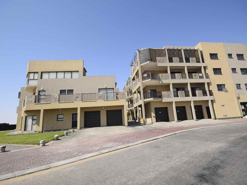 Front elevation of a multi-story apartment complex featuring paved driveway access, integrated garage doors, and private balconies with metal railings.