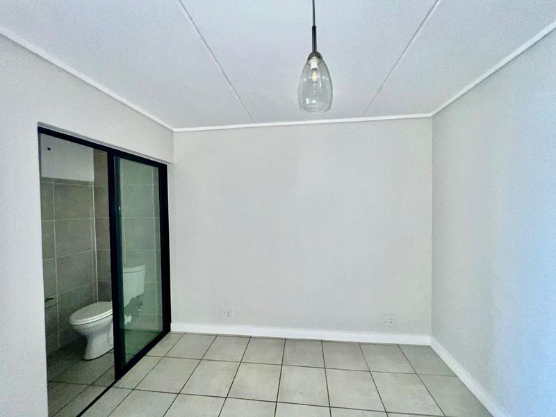 A clean, empty bedroom featuring neutral tiled flooring, a modern pendant light, and a sliding glass door providing a view into the adjacent bathroom.