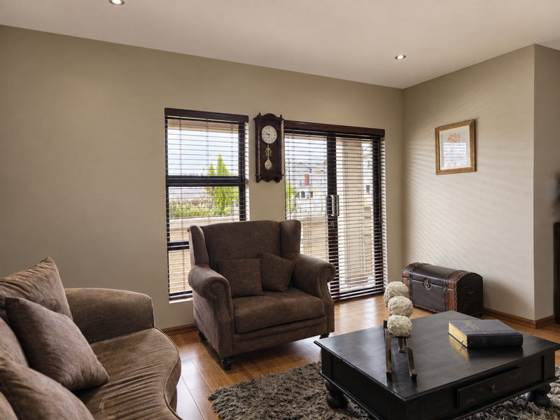 A well-maintained living room featuring laminate flooring, recessed downlights, and sliding glass doors with venetian blinds providing natural light.