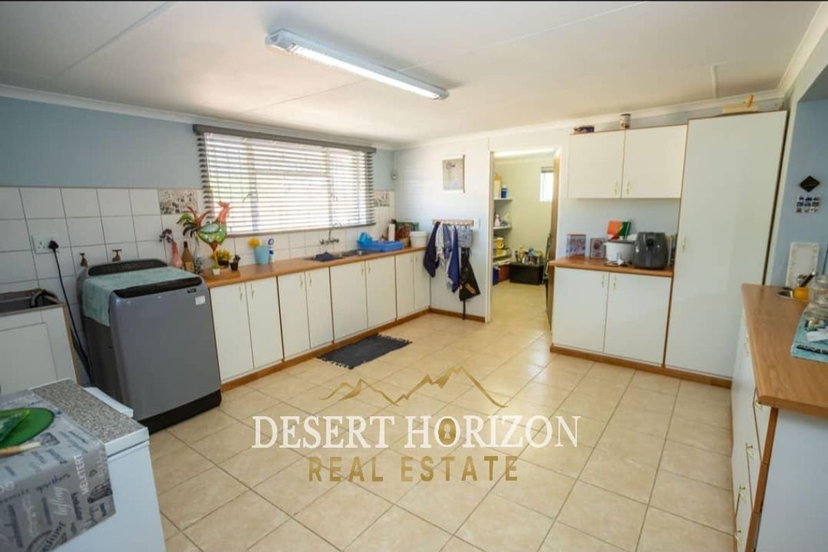 Functional kitchen featuring white cabinetry, tiled splashbacks, and a dedicated laundry area with direct access to a scullery or pantry space.
