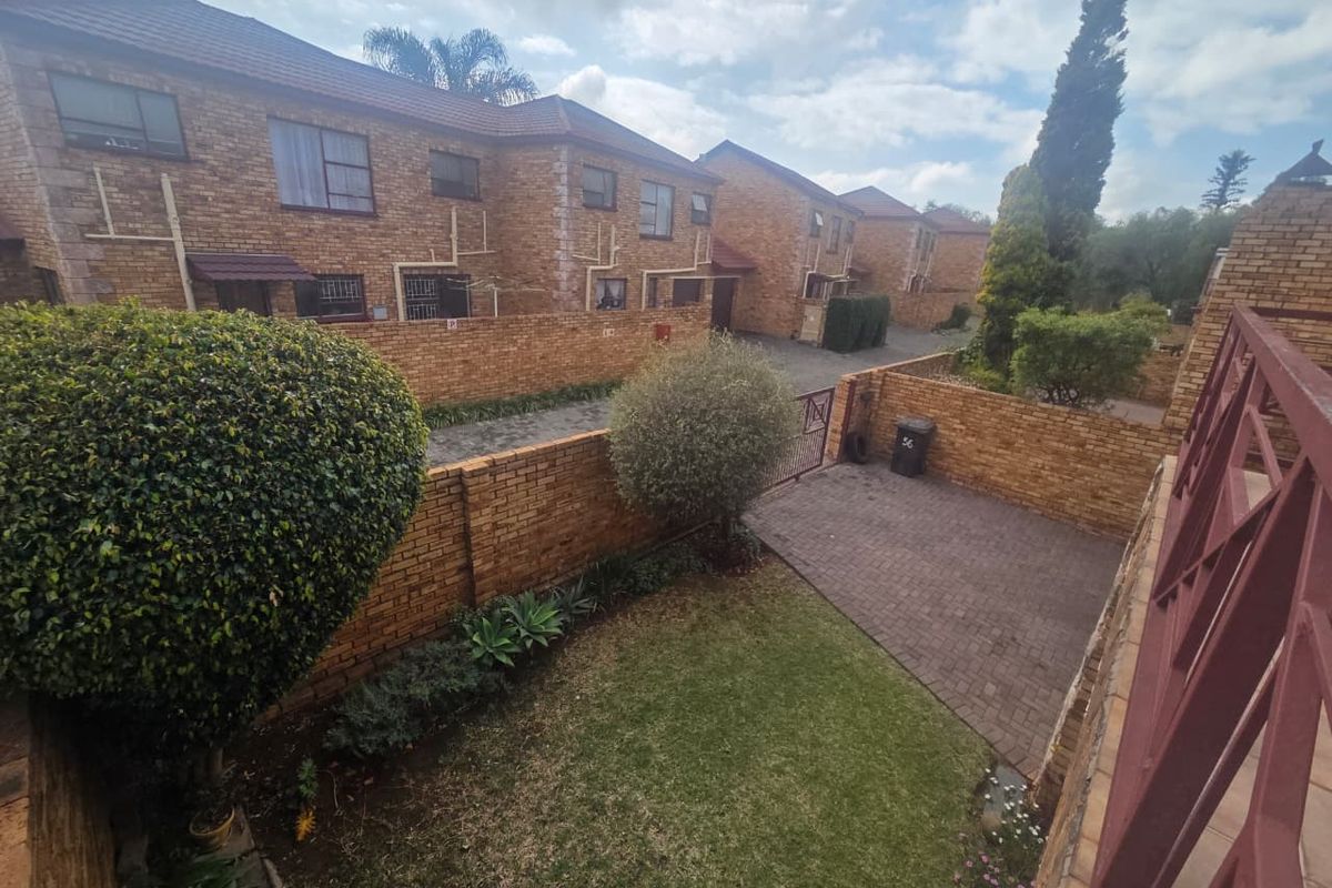An elevated view of a townhouse complex rear courtyard featuring a private garden, brick paved driveway, and secure boundary walling.
