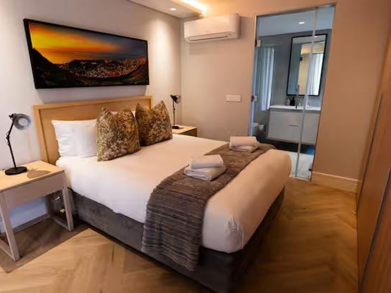 Modern bedroom featuring herringbone timber flooring, built-in wardrobe, wall-mounted air conditioning, and an en-suite bathroom with a glass partition.