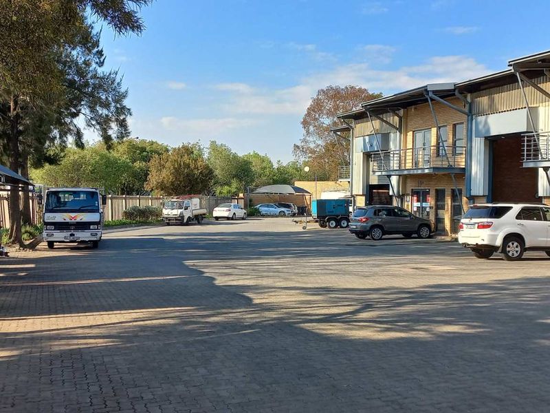 Exterior view of an industrial property featuring a paved parking area, covered parking bays, and multi-level office or warehouse units with balconies.