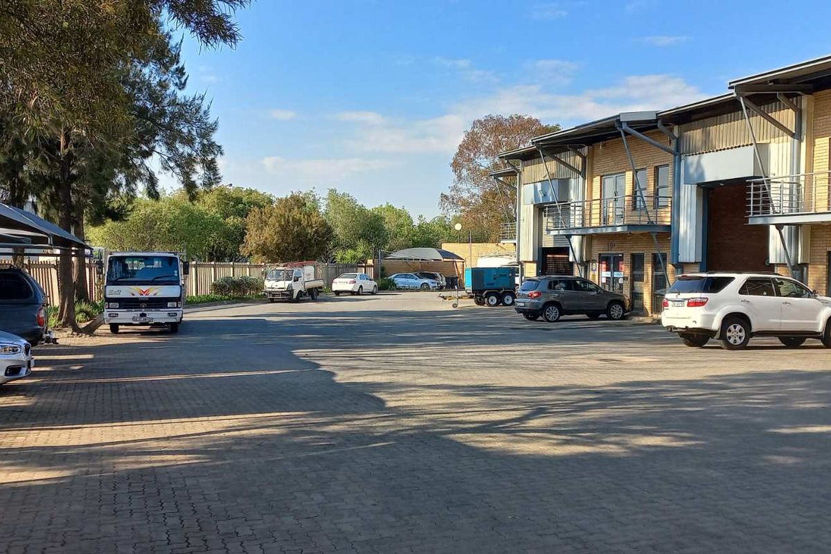Exterior view of an industrial property featuring a paved parking area, covered parking bays, and multi-level office or warehouse units with balconies.