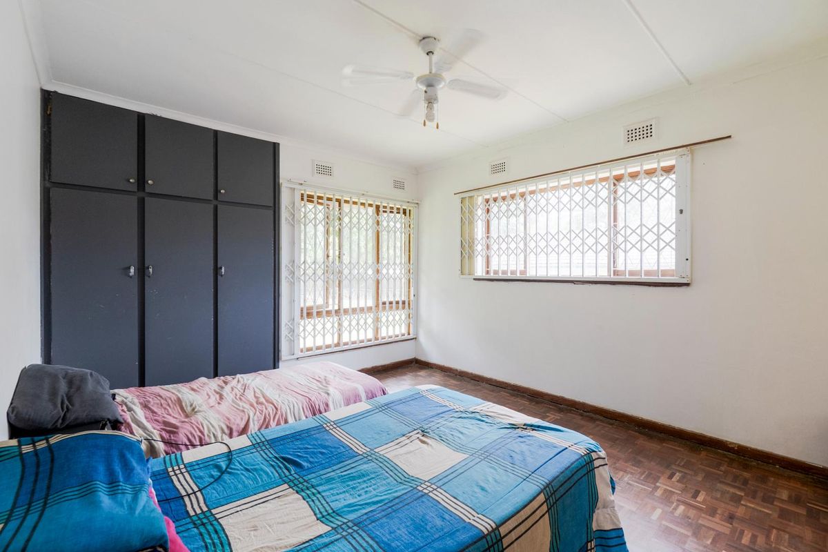 A bedroom featuring parquet flooring, built-in cupboards, and security bars on the windows.