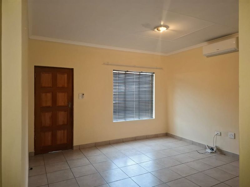 An empty living room featuring neutral wall paint, tiled flooring, an installed air conditioning unit, and a wooden door.