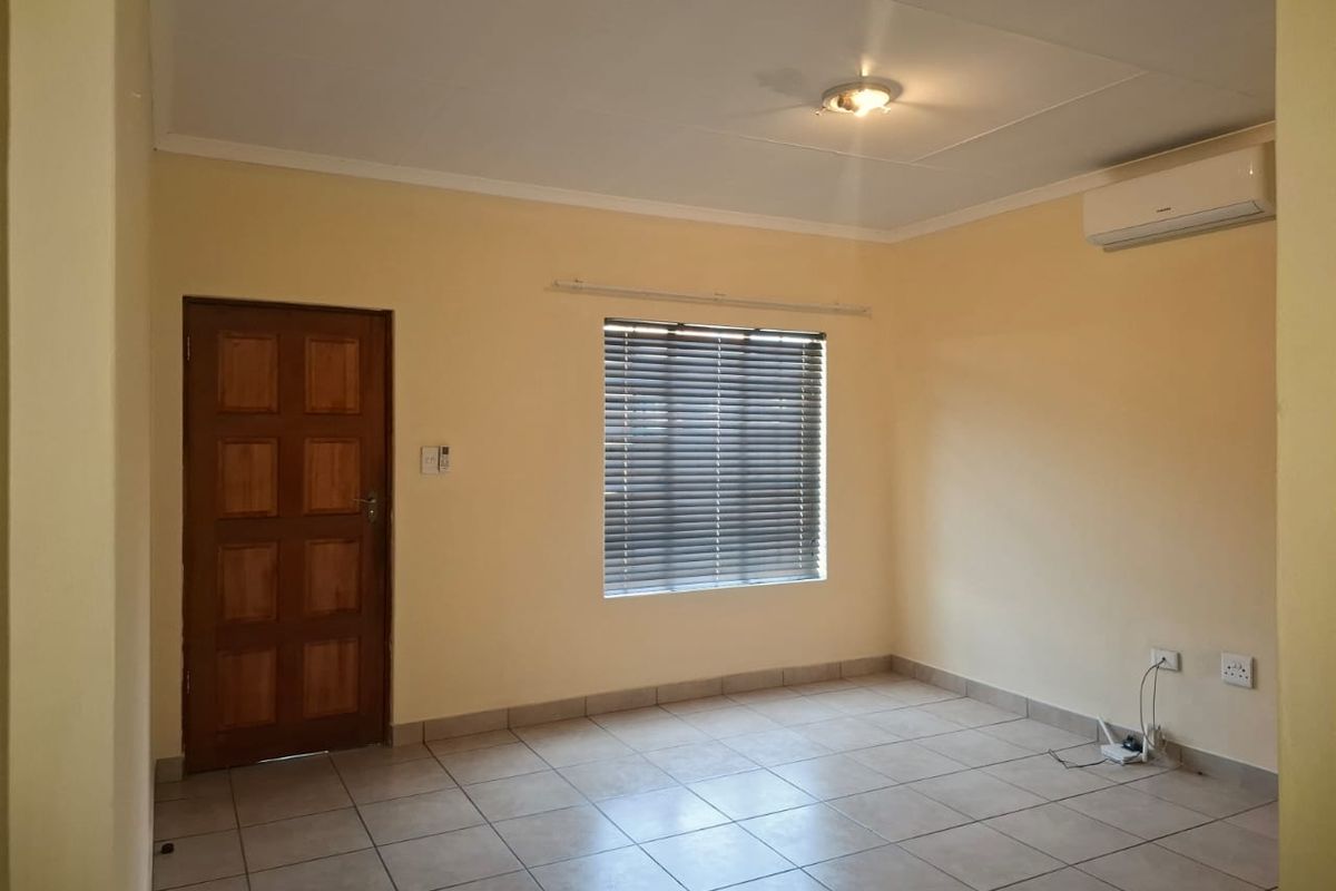 An empty living room featuring neutral wall paint, tiled flooring, an installed air conditioning unit, and a wooden door.