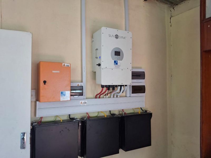 Utility area featuring a wall-mounted solar inverter and battery storage system with associated electrical distribution boards.