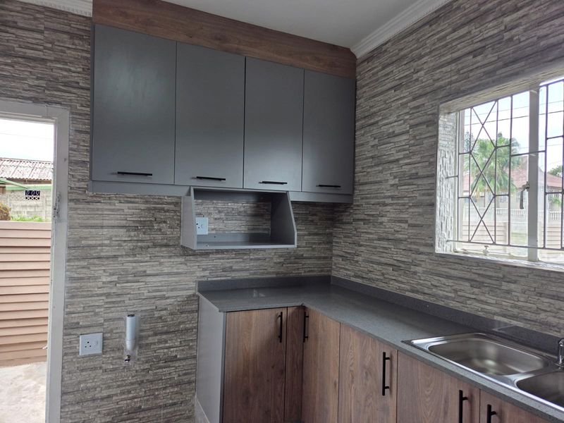 A modern, empty kitchen featuring two-tone cabinetry, stone-look wall finishes, and a stainless steel sink with a window view.
