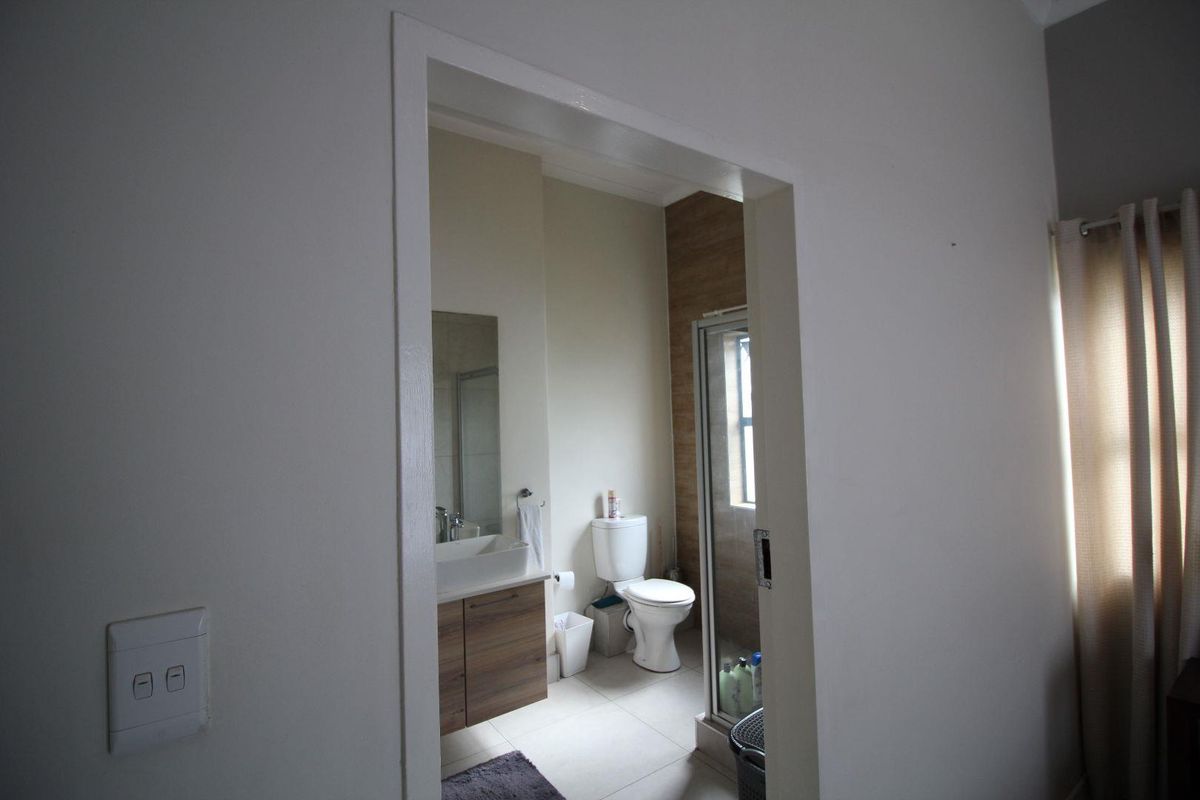 A view into a compact bathroom featuring a modern vanity with basin, a toilet, and a glass-enclosed shower with wood-look wall tiling.