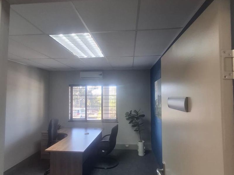 A professional office suite featuring carpeted flooring, a suspended ceiling with recessed lighting, and a wall-mounted split-system air conditioner.