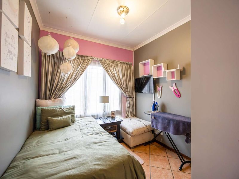 A compact bedroom featuring tiled flooring, neutral wall tones with a pink accent wall, and large windows with curtain treatments.