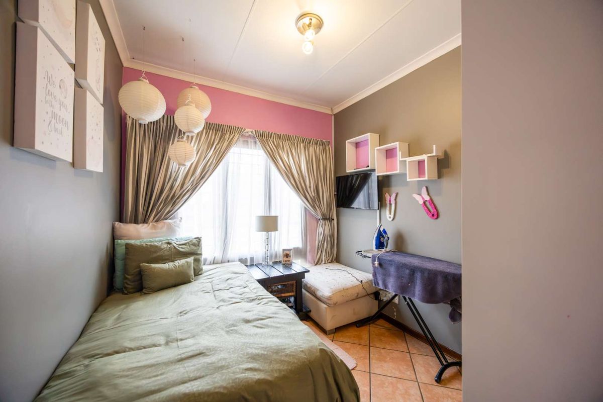A compact bedroom featuring tiled flooring, neutral wall tones with a pink accent wall, and large windows with curtain treatments.