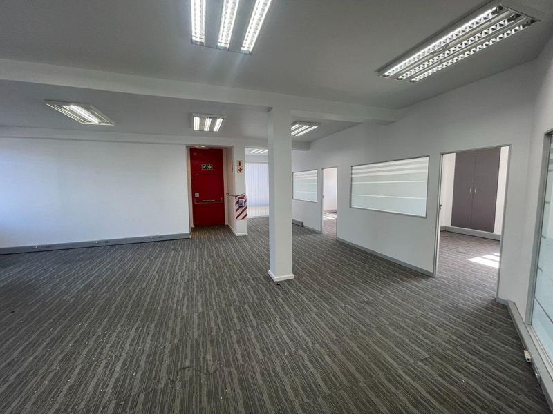A spacious, open-plan office area featuring neutral carpeting, recessed fluorescent lighting, and internal glass partitions, providing a clean and professional workspace environment.