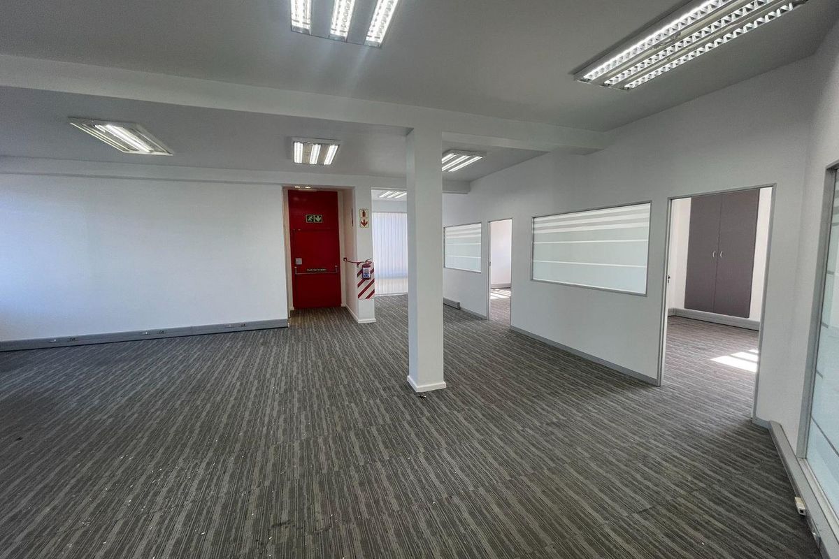 A spacious, open-plan office area featuring neutral carpeting, recessed fluorescent lighting, and internal glass partitions, providing a clean and professional workspace environment.