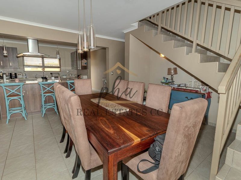 Open plan dining area adjacent to a modern kitchen with island, featuring tiled floors and a staircase with integrated balustrade.