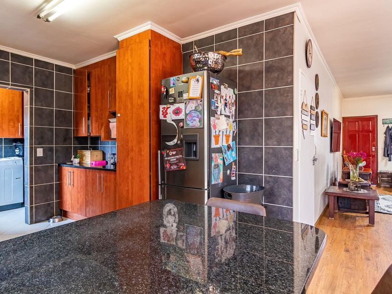 Open plan kitchen and living area featuring granite countertops, wooden cabinetry, and a separate scullery space with tiled finishes.