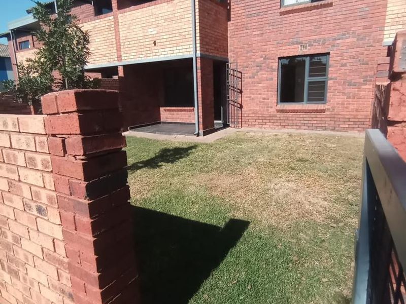 Rear view of a townhouse featuring a private garden, brick boundary wall, and an upper-level balcony with face brick exterior.