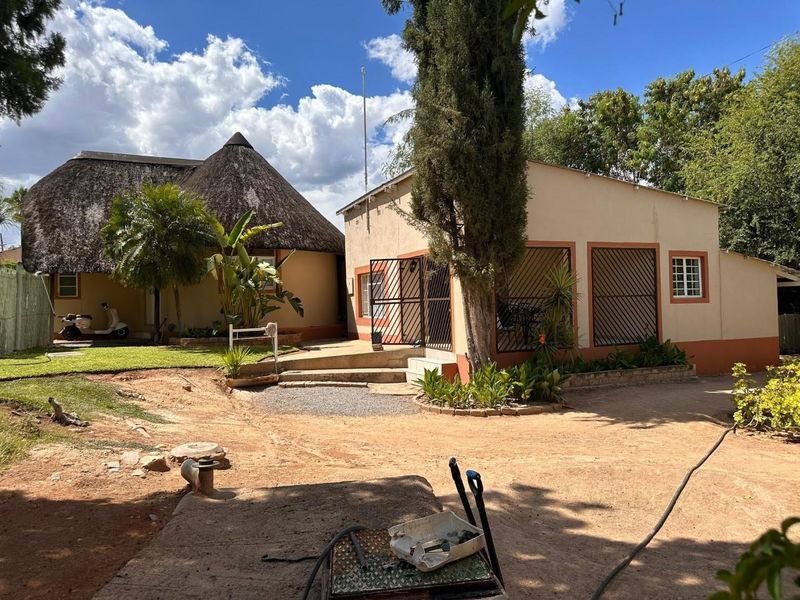 Rear view of the property featuring a traditional thatch roof structure and a secondary building with security gates and bars.