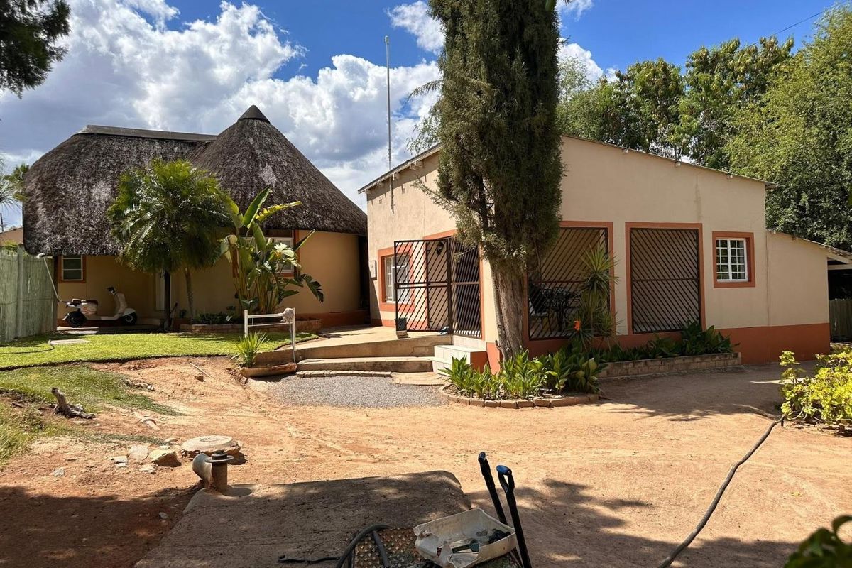 Rear view of the property featuring a traditional thatch roof structure and a secondary building with security gates and bars.