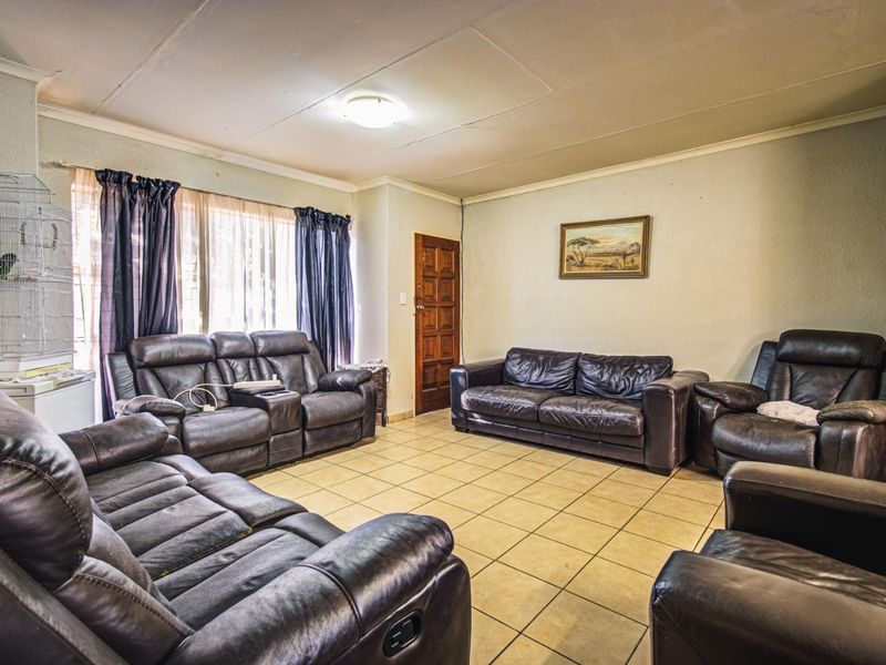 A spacious living room featuring tiled flooring, a flush mount ceiling light, and a traditional wooden door, offering a functional layout for family living.
