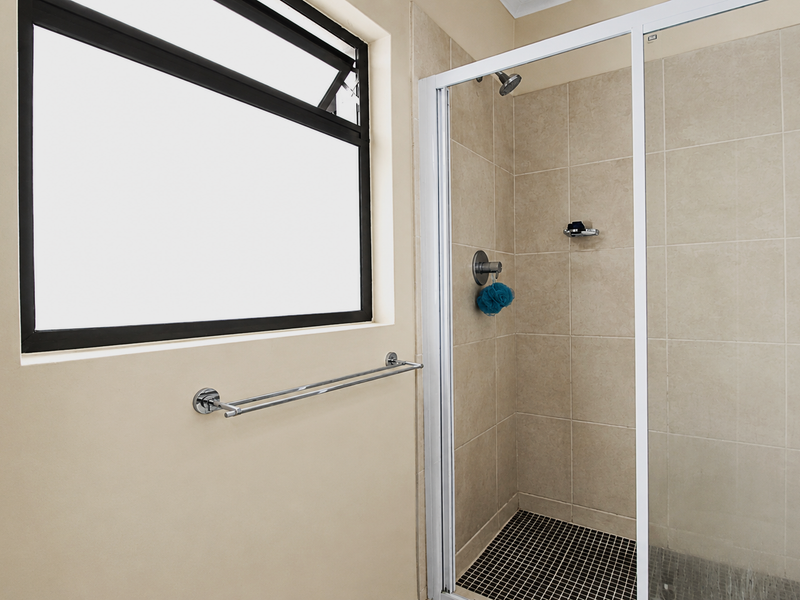 A clean, functional bathroom featuring a tiled shower enclosure with a glass door, a modern towel rail, and a window for natural light.