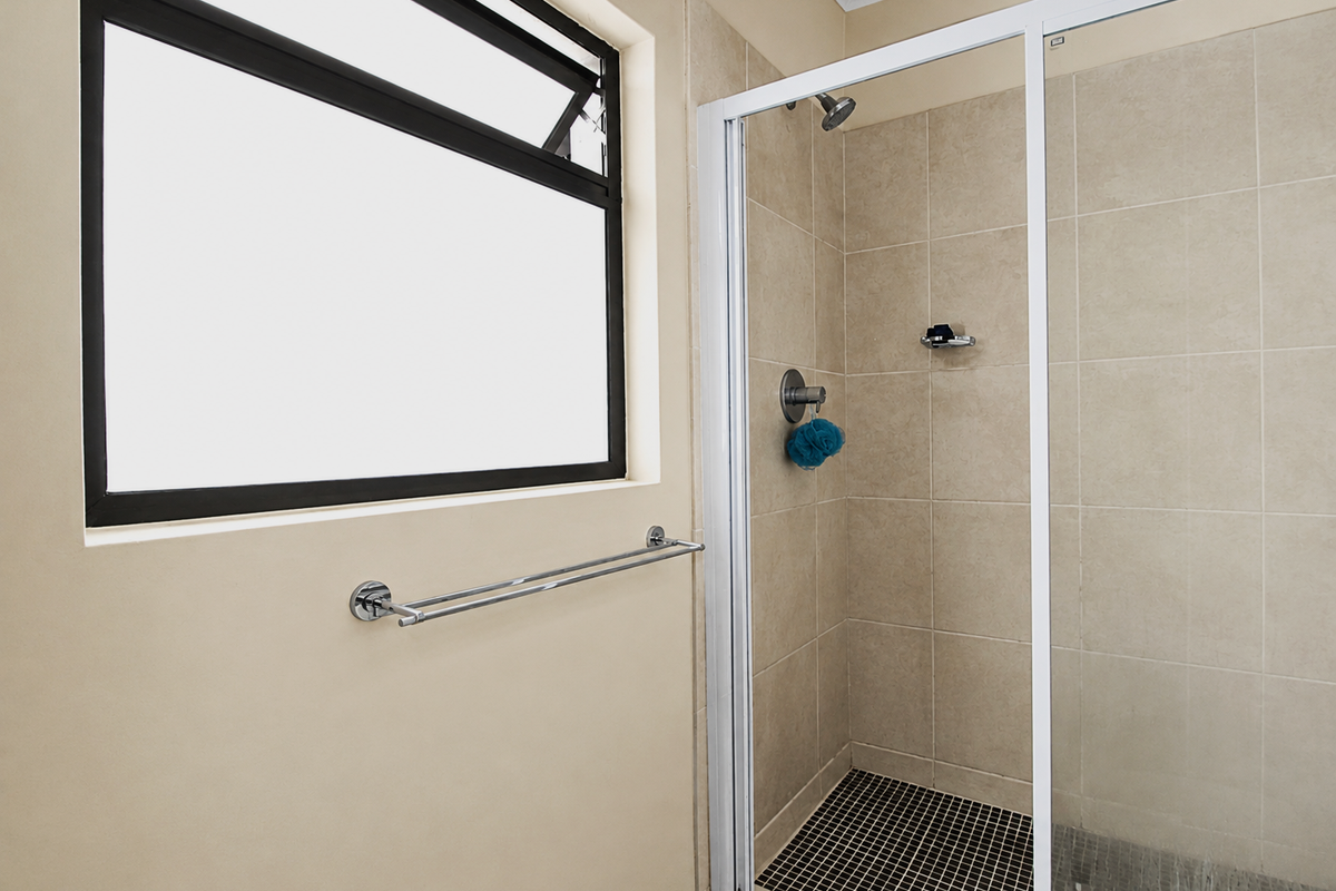 A clean, functional bathroom featuring a tiled shower enclosure with a glass door, a modern towel rail, and a window for natural light.
